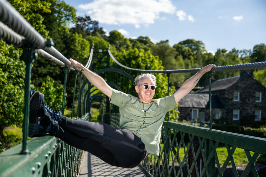 Alan Cumming swinging on a bridge