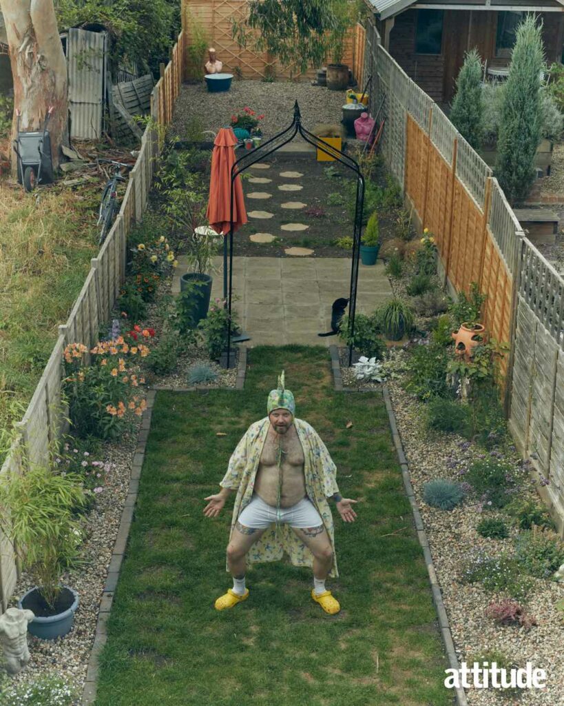 Ginny Lemon standing in their garden wearing white boxer shorts and a lizard hat