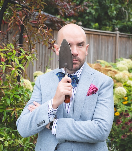 Tom Allen in a light blue suit holding onto a spade in a garden