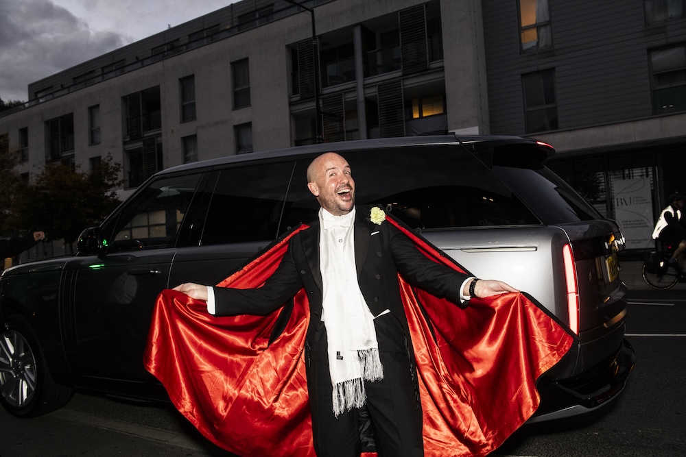 Tom Allen in a red cape and black suit on the street