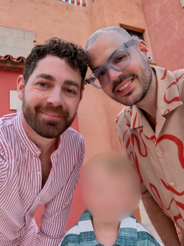 Derry and Morgan with their son, whose face is blurred, standing infant of an outdoor wall