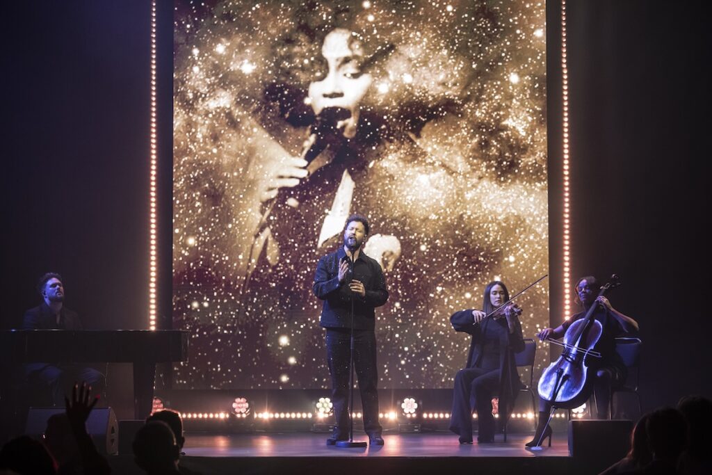 Callum Scott singing on stage with an image of Whitney on the screen behind him