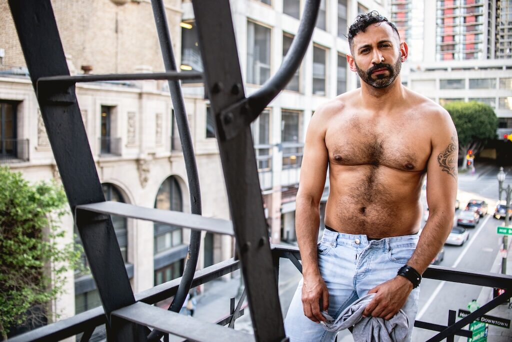 Alan Adolfo, topless in jeans, standing on a stairwell, bearded