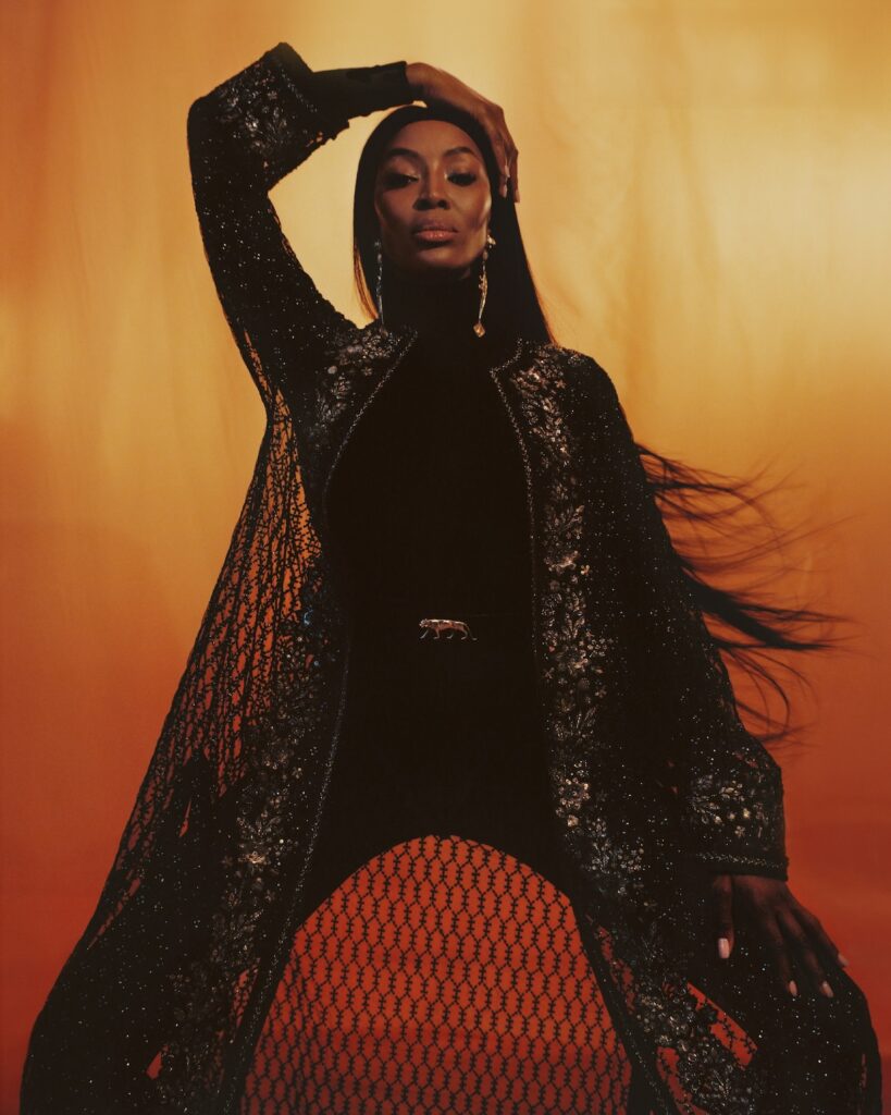 Naomi Campbell photographed by Campbell Addy, Naomi against an organ backdrop in a black lace trouser, top and see-through jacket combo