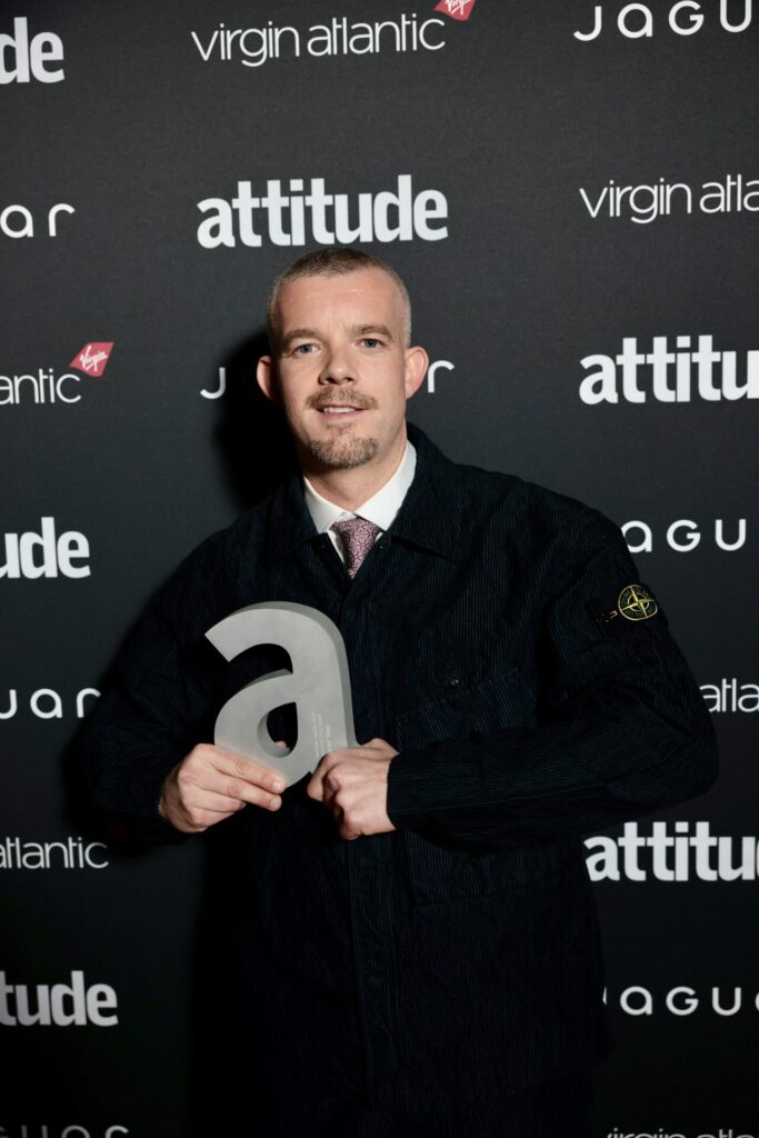 Russell Tovey in a collar and tie and dark top holding award