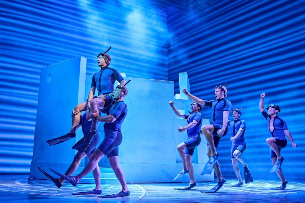 Male ensemble lifting a performer during a high-energy scene in Mamma Mia!