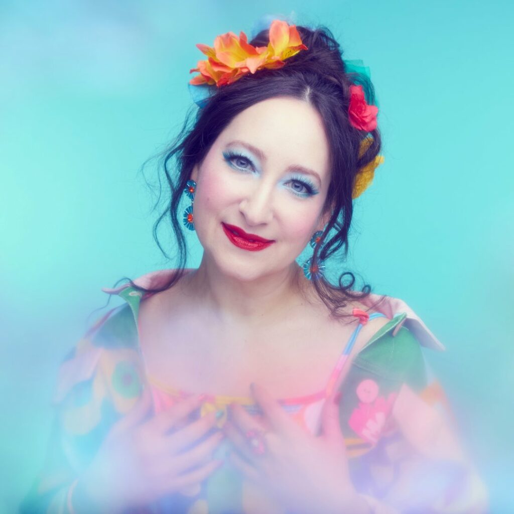 Rachael Sage wearing a colourful outfit against a blue backdrop