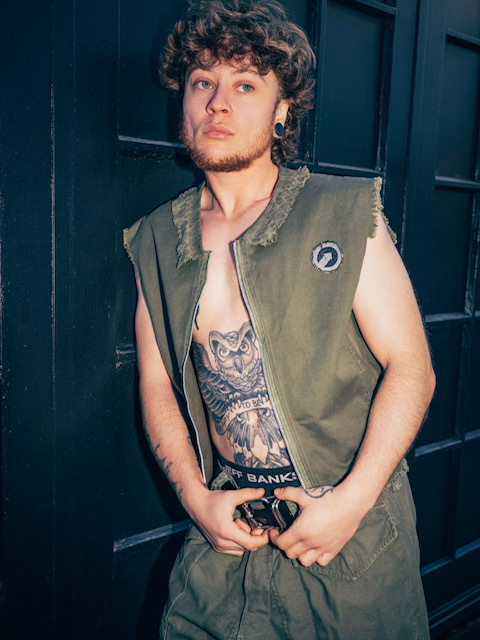 Greyson X A Kempster in sleeveless green top holding onto his belt