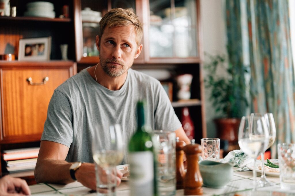 Alexander skarsgaard in a grey t-shirt sitting eating a meal in Pillion still