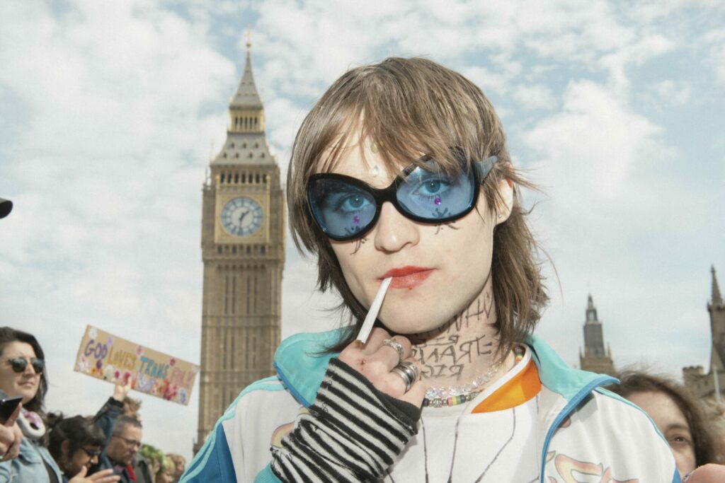 A protester standing in-front of Big Ben wearing blue glasses smoking a cigarette 