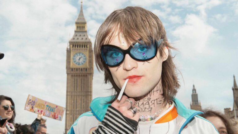 A protester standing in-front of Big Ben wearing blue glasses smoking a cigarette