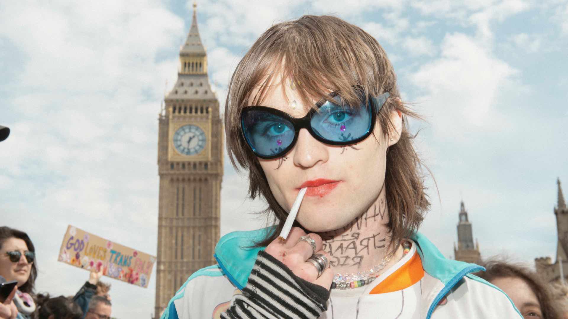 A protester standing in-front of Big Ben wearing blue glasses smoking a cigarette