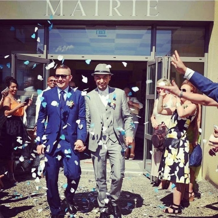Two men in suits holding hands having flower petals thrown over them