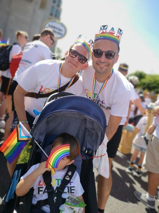Two men in Pride outfits with a child in a pram