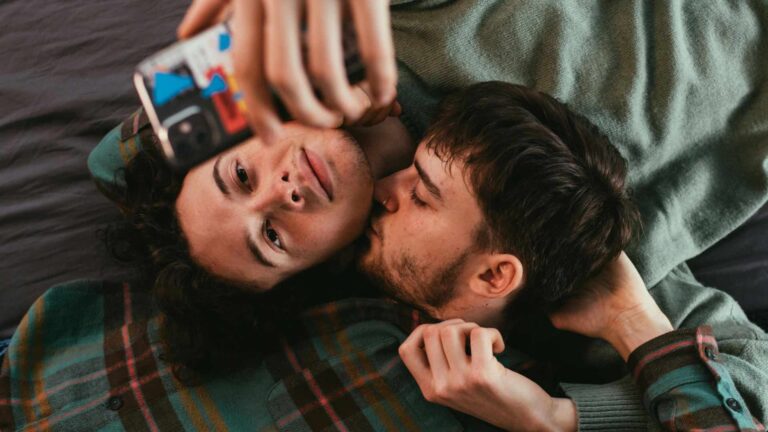 two men in bed on their phone kissing