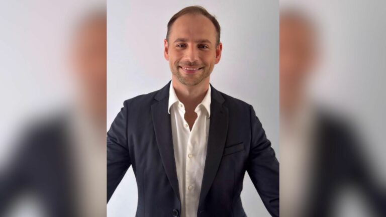 A portrait shot of a smiling man in a blue jacket and white shirt