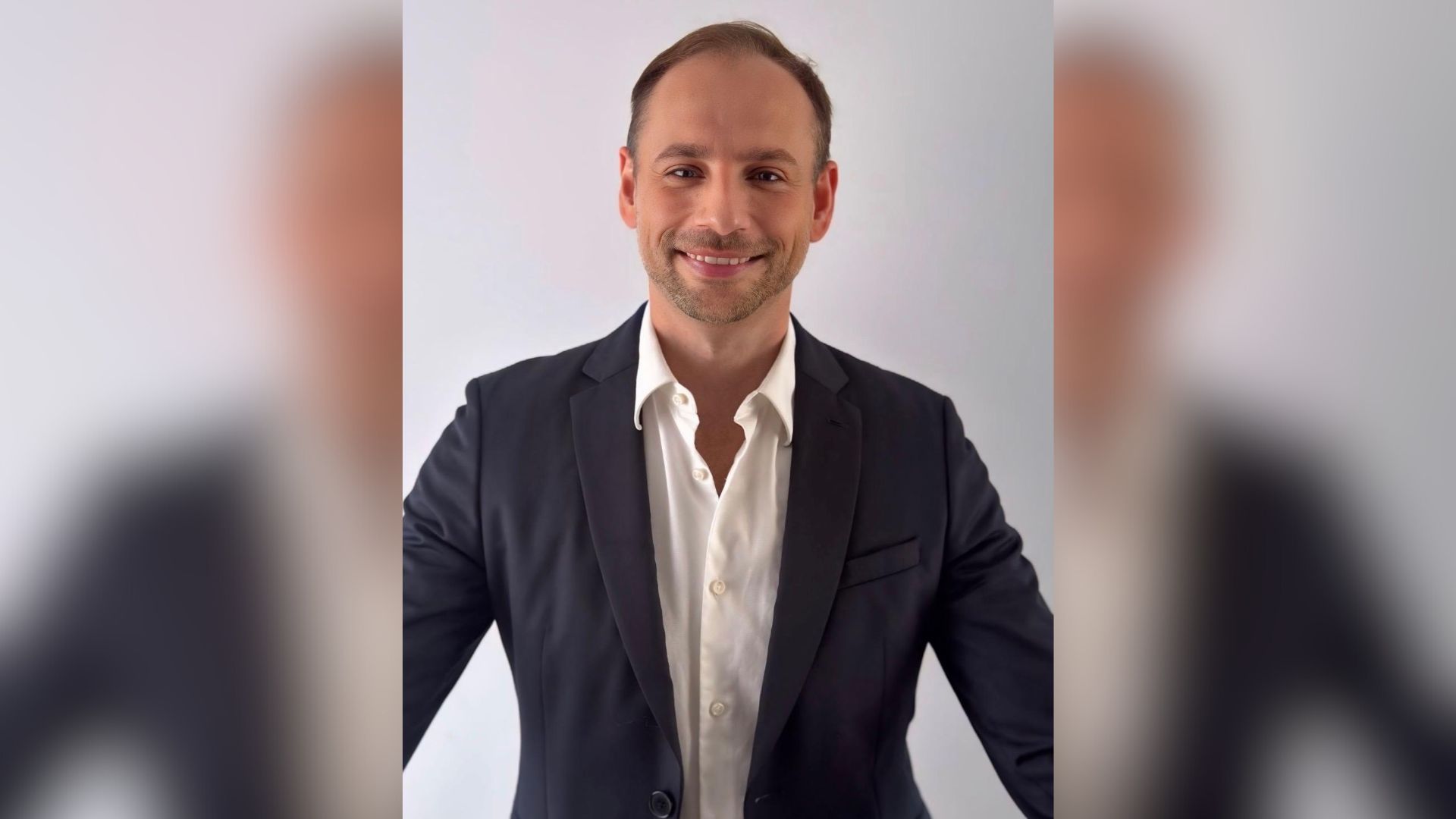A portrait shot of a smiling man in a blue jacket and white shirt