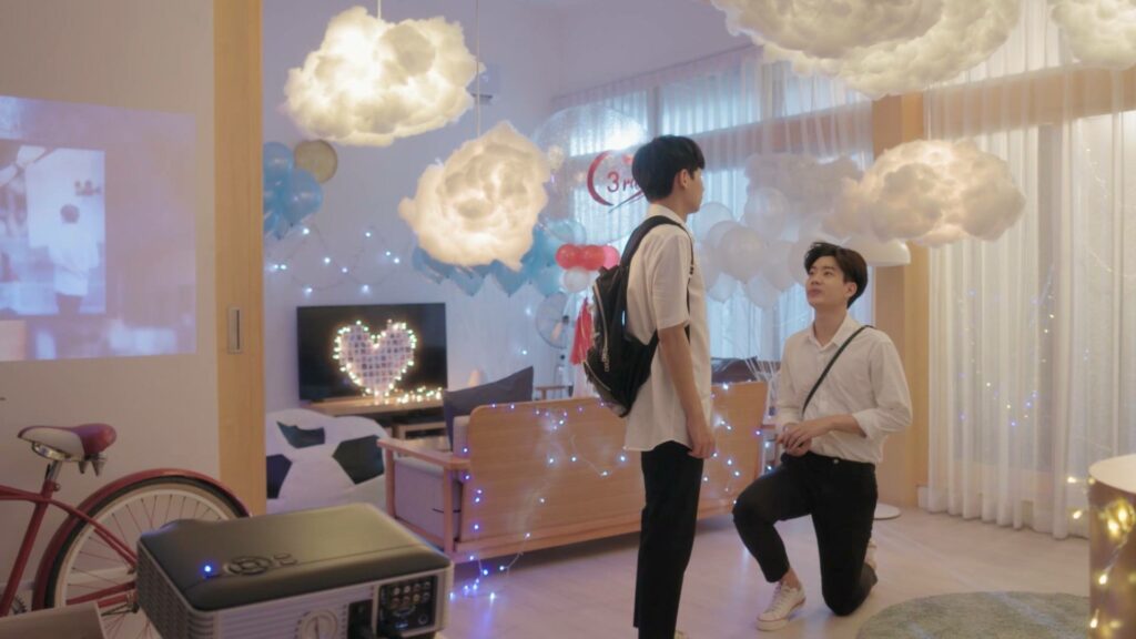 A scene from Thai BL series Theory of Love showing one character kneel down in front of another one