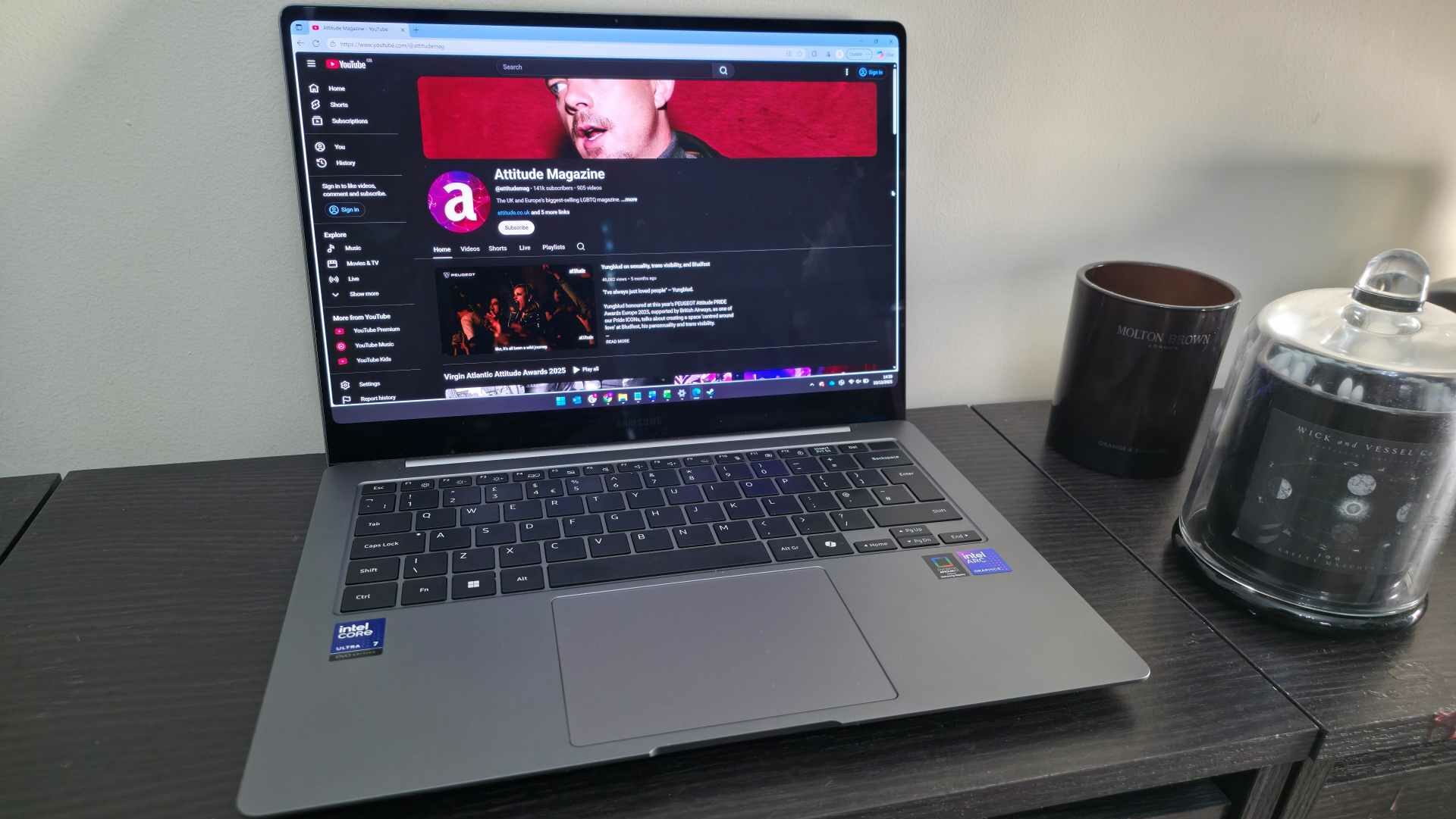 A Samsung laptop sitting on a black shelf with a candle next to it