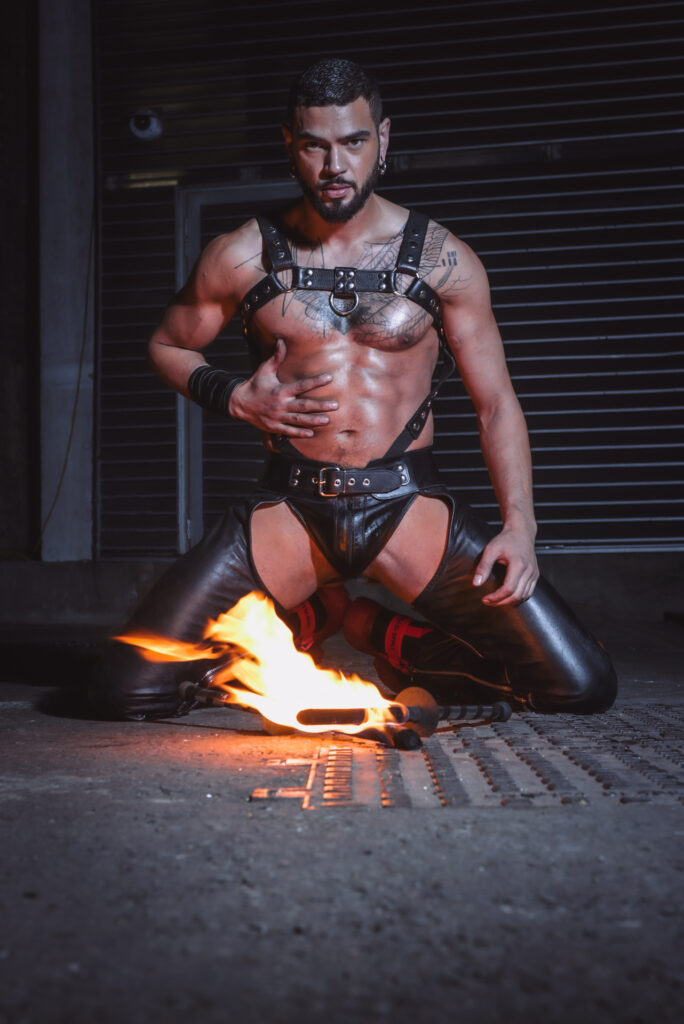 Sadiq Ali in a leather harness with fire in-between his legs