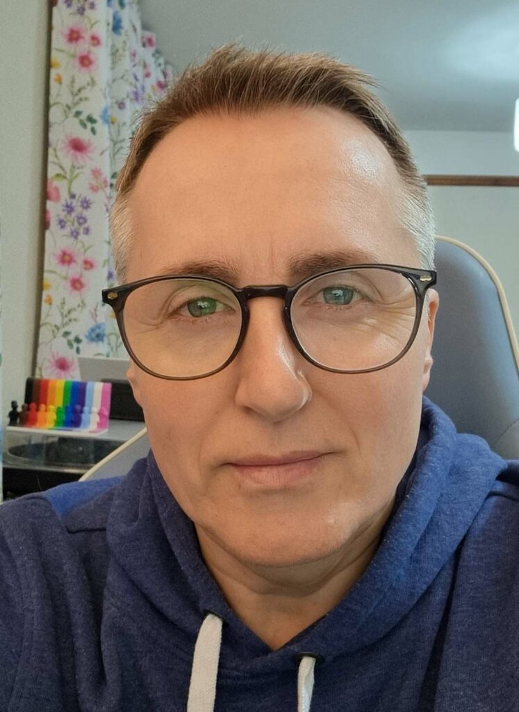 A portrait shot of a smiling man wearing black glasses