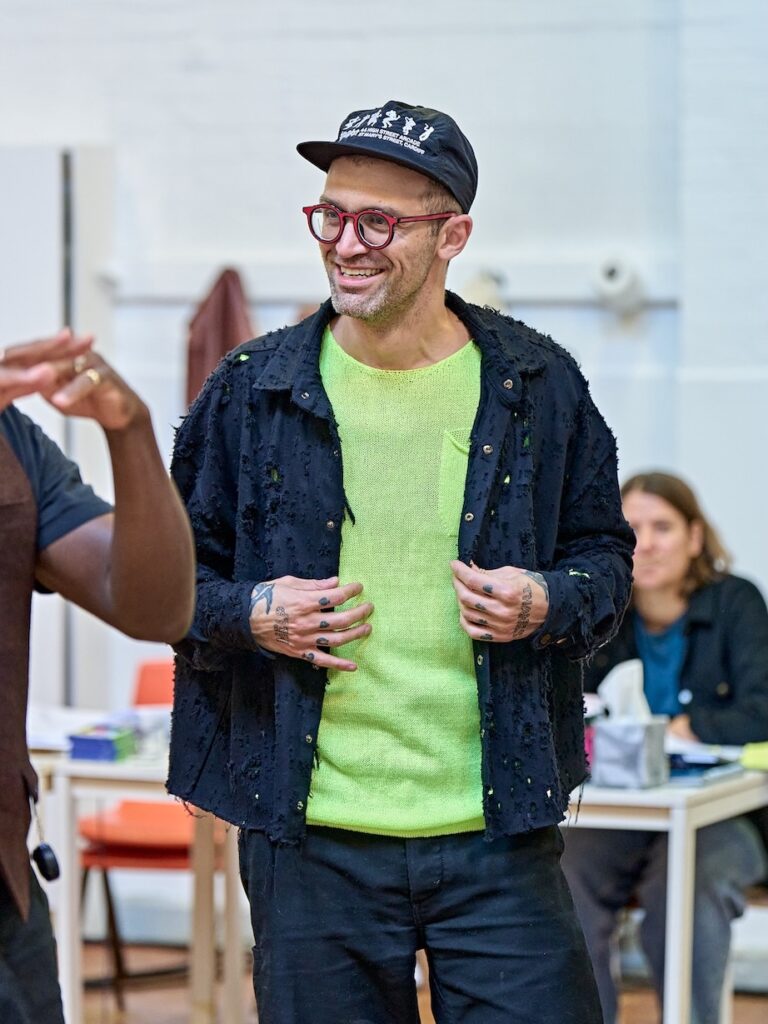 Sam Pinkleton in rehearsal in a blue jacket and green jumper