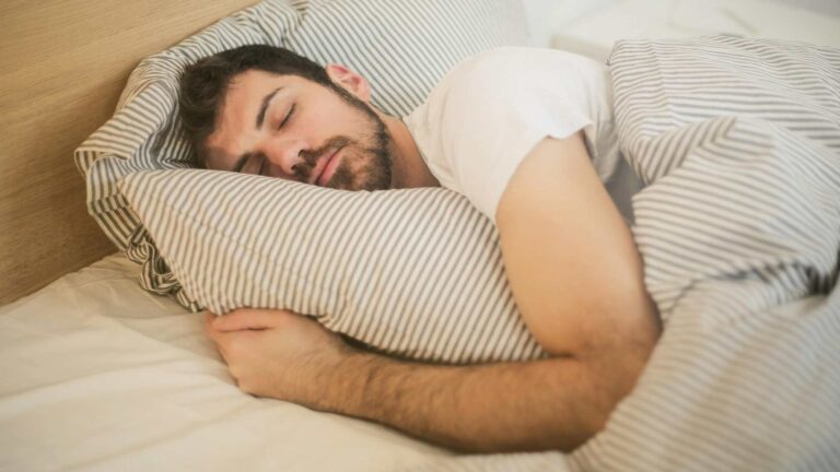 A sleeping man in a bed wearing a white T-shirt