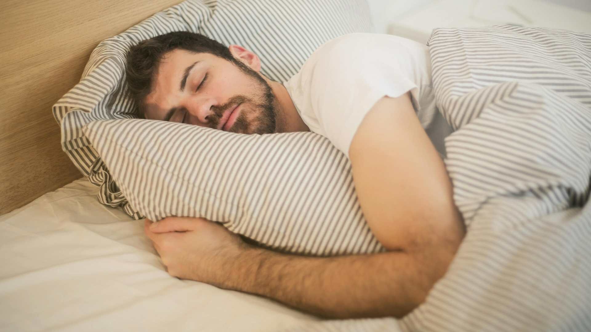 A sleeping man in a bed wearing a white T-shirt