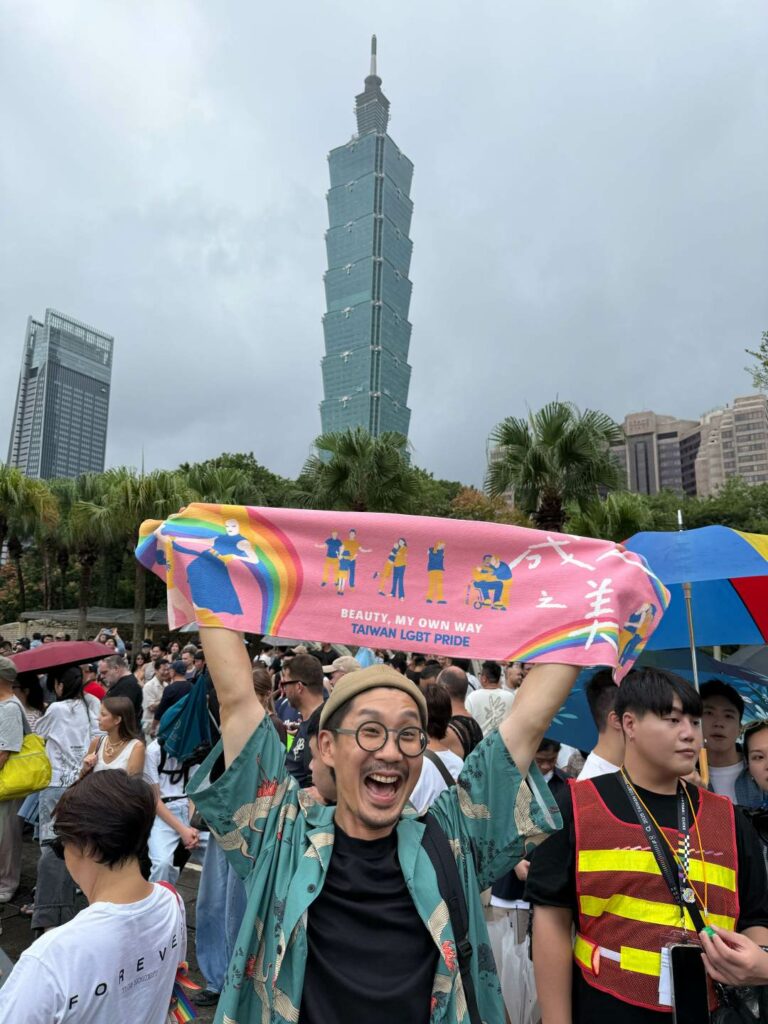 A person waving a pink banner in front of the Taipei 101 during Taiwan Pride 2025