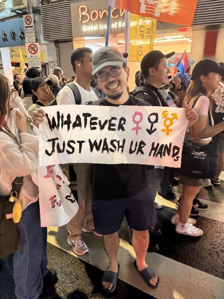 A person holding a sign saying "Whatever. Just wash your hands" during the Trans march at Taiwan Pride 2025