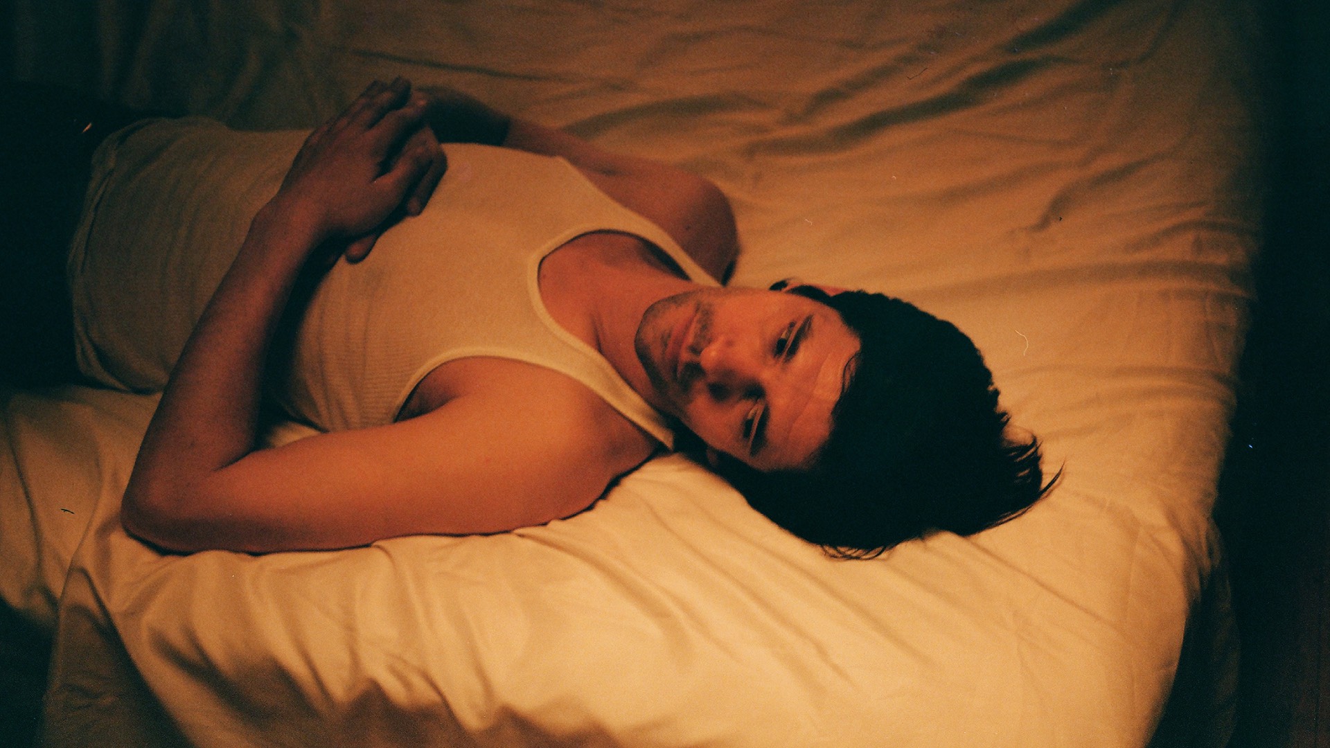 Ben Whishaw in Peter Hujar's Day, lying on a bed in a white vest bathed in orange light