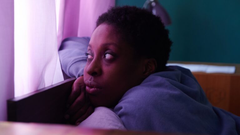 A character from the film Dreamers peering through a window and bathed in purple light