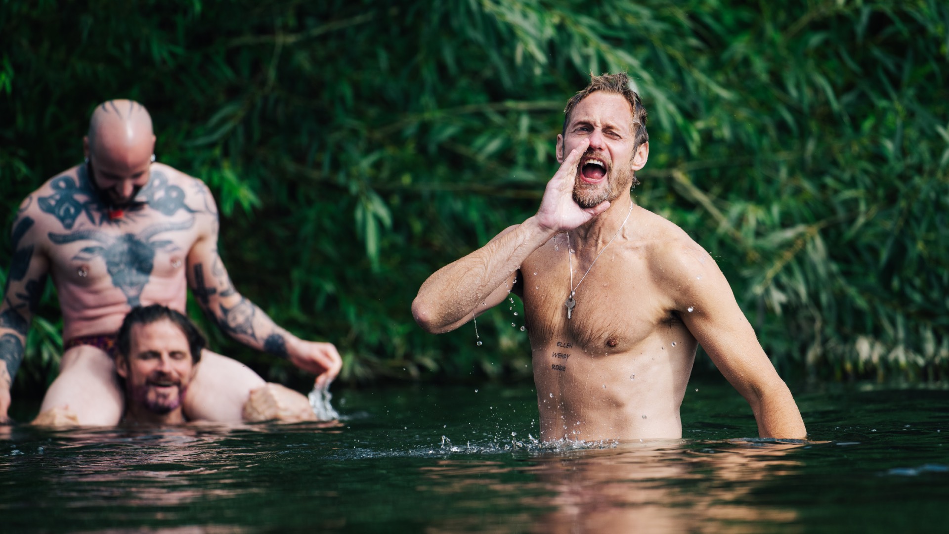 Alexander and two extras frolicking in a pond in a photo from the set of Pillion