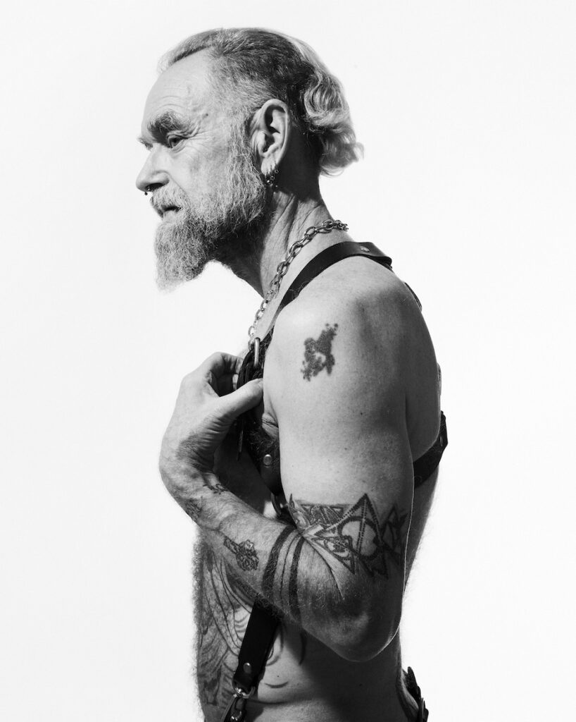 a model for Matt Ford posing topless from the side wearing leather harness