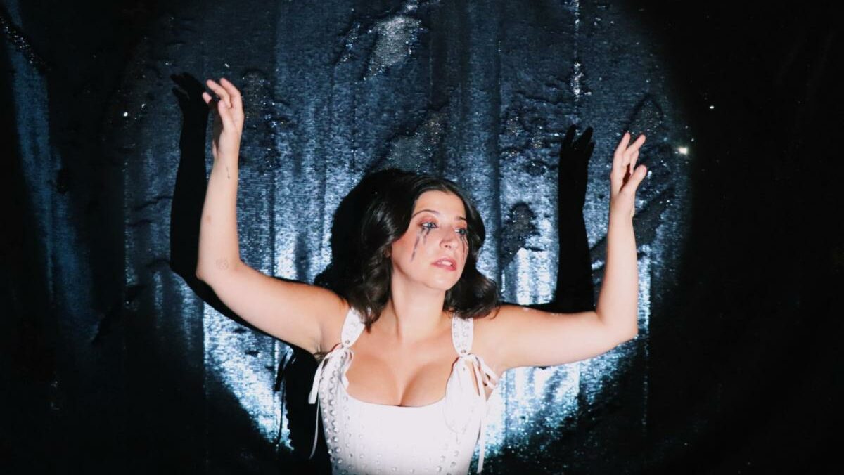 Ariana and the Rose wearing a white top against a black backdrop