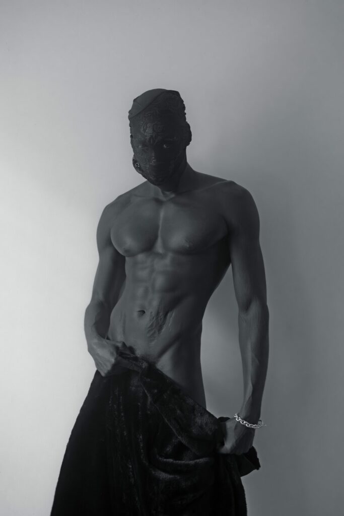 A black and white photograph by Michael Epps showing a topless model in a black mask