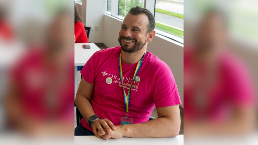 Mohamed Amine Guerfali smiling while seated at a desk, wearing a pink T-shirt and lanyard.