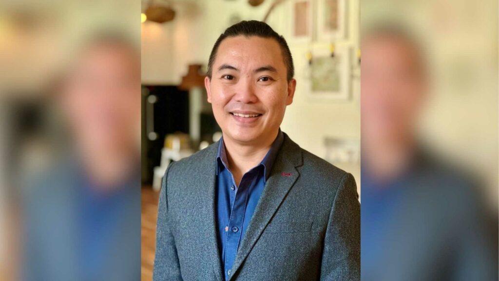 Edison Chen smiling, wearing a blue shirt and blazer, standing indoors.