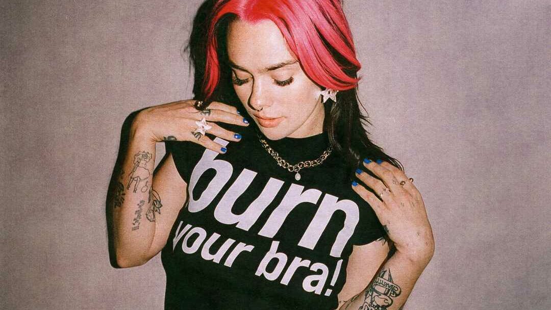 A woman with pink hair wearing a T-shirt that says burn your bra on it