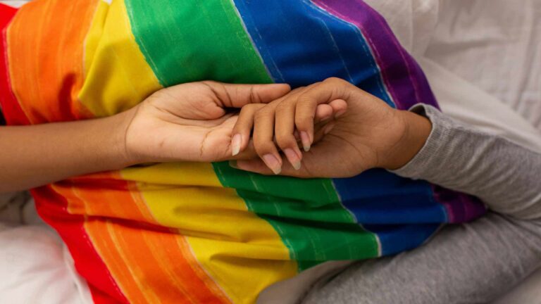 couple holding hands in front of LGBTQ+ flag