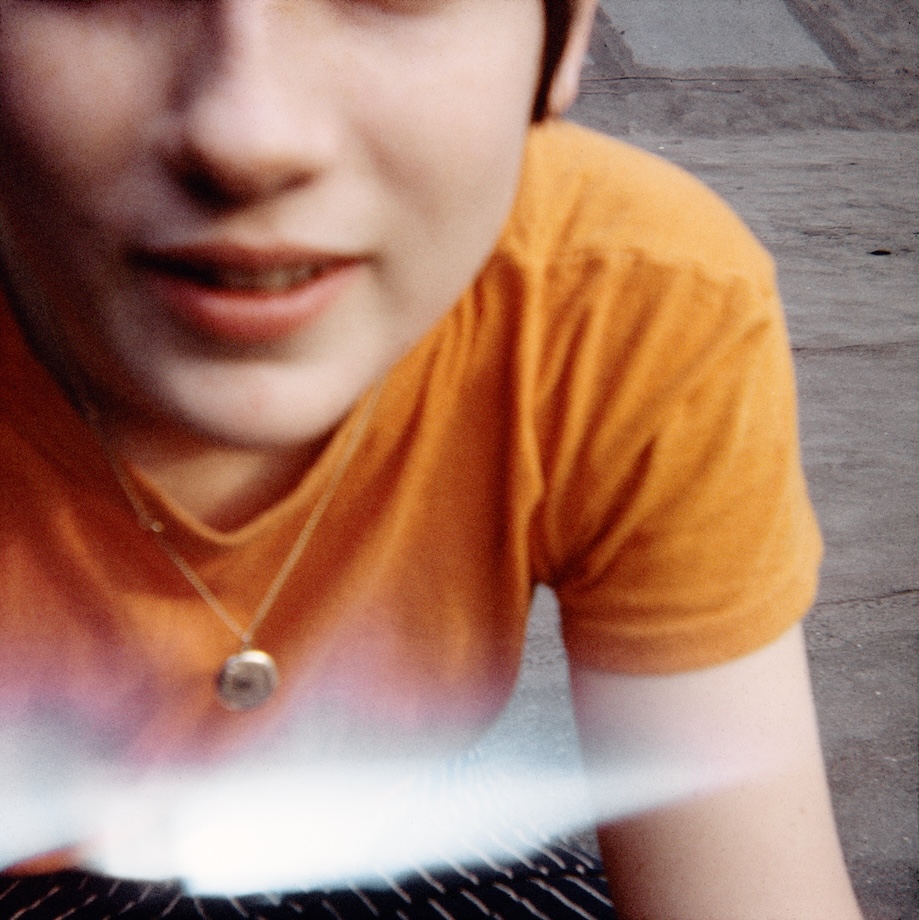 a sitter in an orange t-shirt leasing towards camera and smiling, head cut off above the nose