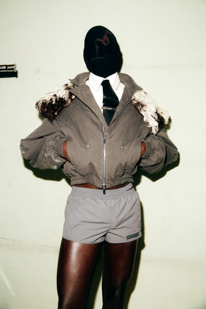 A model wearing a fur collared bomber jacket, grey boxer shorts and face mask waits backstage at the LGN Louis Gabriel Nouchi Autumn/Winter 2026 runway show at Paris Fashion Week