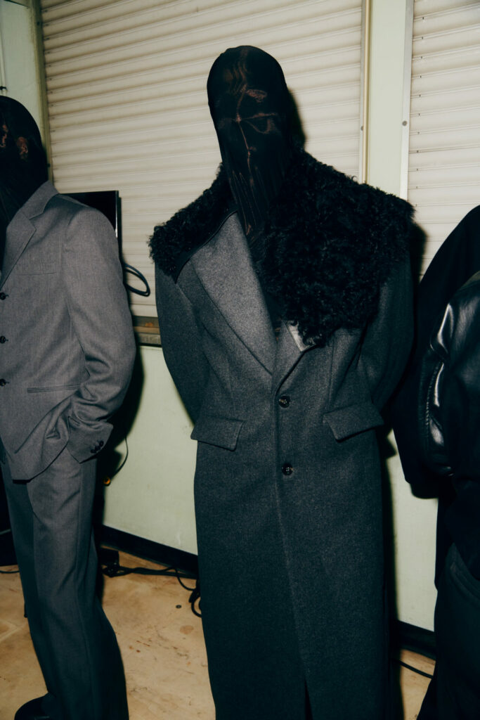 A model wearing a fur collared wool overcoat and face mask waits backstage at the LGN Louis Gabriel Nouchi Autumn/Winter 2026 runway show at Paris Fashion Week