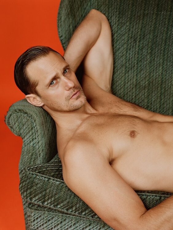 Alexander Skarsgård lying down on a green chair topless, with his arm flexed behind his head