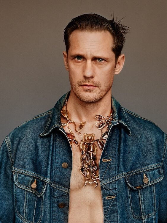 Alexander Skarsgård wearing an open denim jacket with a gold flamboyant necklace