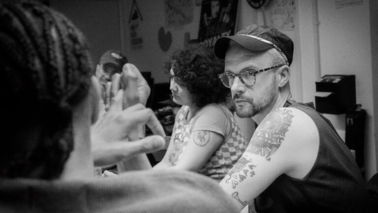 The author Dan Glass at an ACT UP London meeting with other attendees, sat at table, black and white