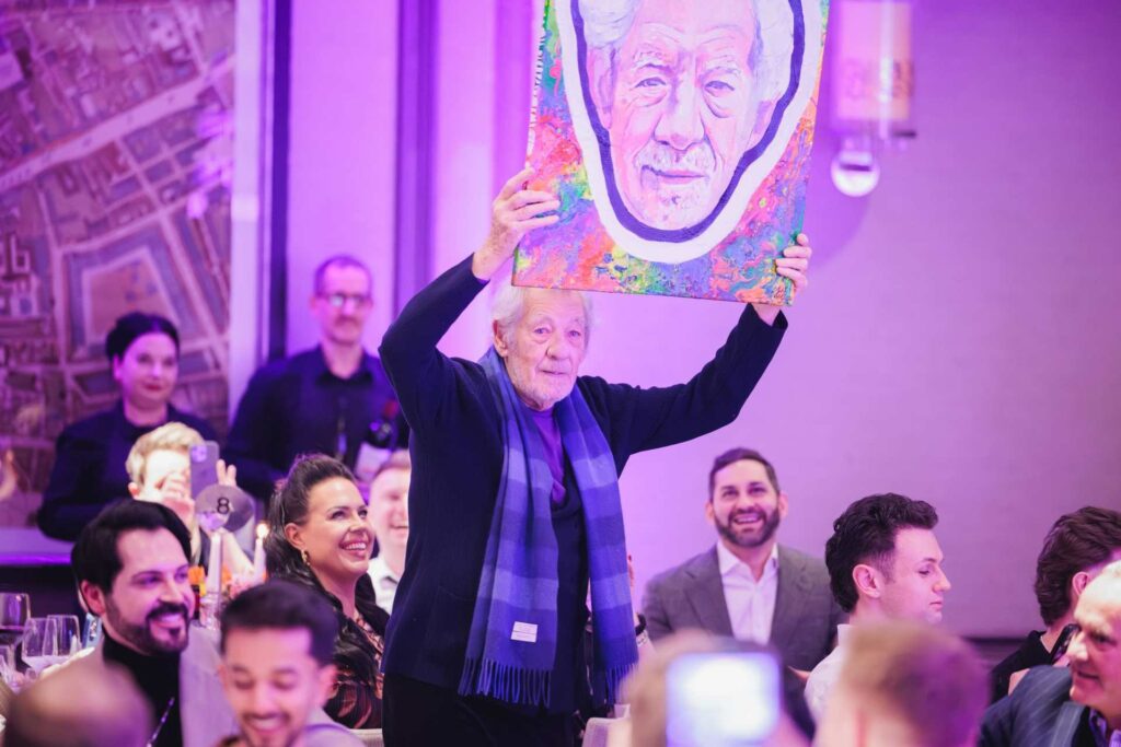 Ian McKellen holding up a painting at the Attitude 101 event