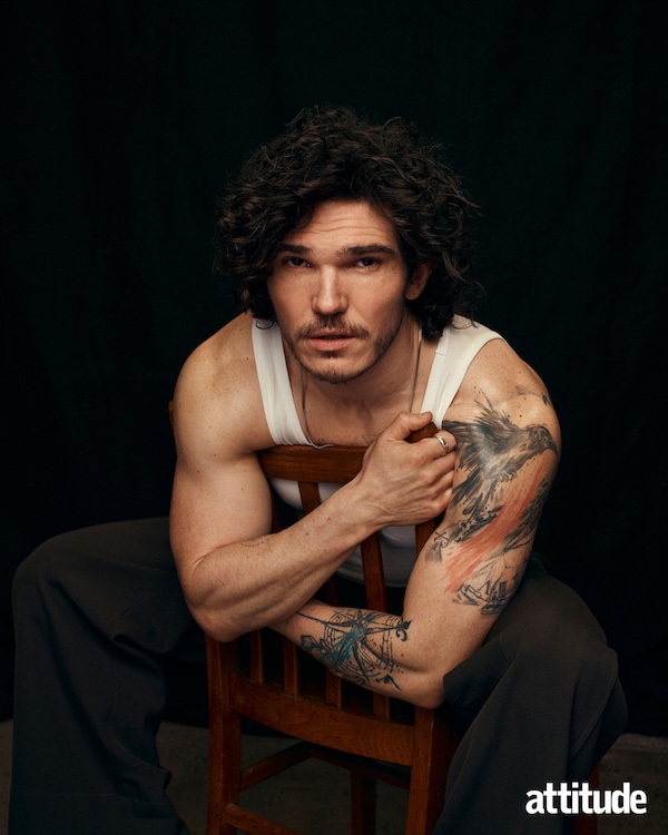 Fra Fee, wearing a white vest hugging the back of a chair he is sat on