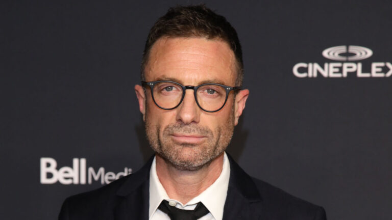 Jacob Tierney in a white shirt and black tie under a black blazer, paired with glasses, on the red carpet