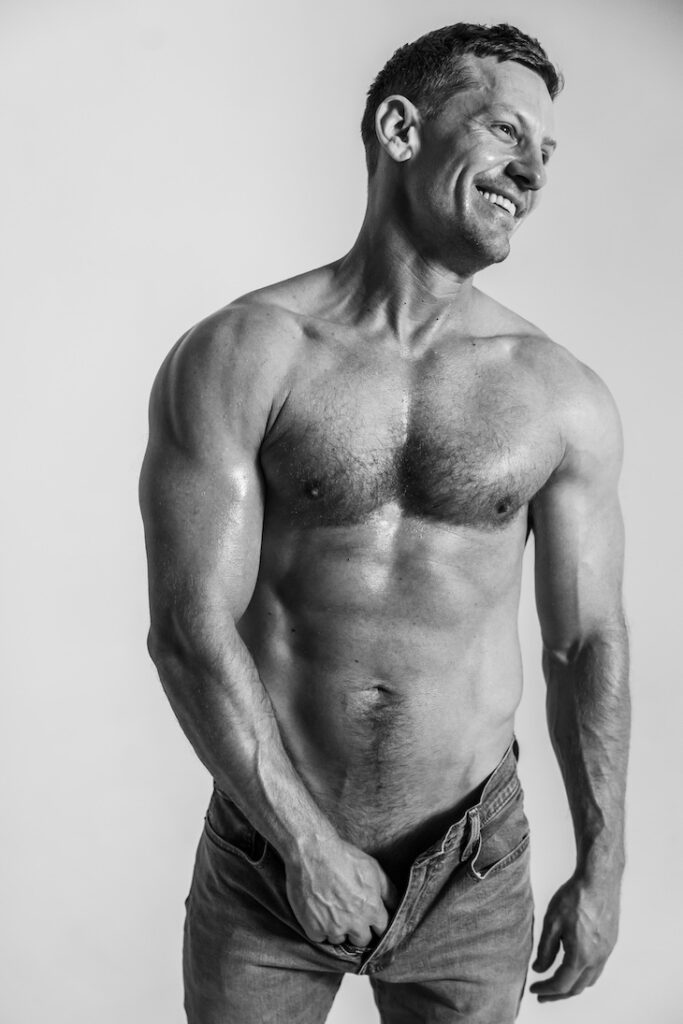 James Sutton shirtless, with his hands down his trousers, in a black-and-white photo